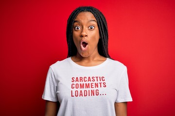 Young african american woman wearing sarcasm coments text on t-shirt over red background scared in...