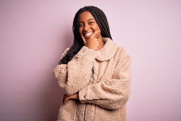 Young african american woman wearing fashion winter coat over pink isolated background looking confident at the camera smiling with crossed arms and hand raised on chin. Thinking positive.