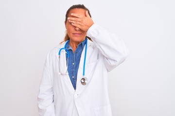 Middle age mature doctor woman wearing stethoscope over isolated background smiling and laughing with hand on face covering eyes for surprise. Blind concept.