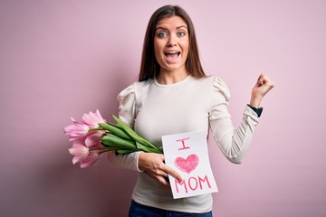 Young beautiful woman with blue eyes holding love mom message and tulips on mothers day screaming proud and celebrating victory and success very excited, cheering emotion