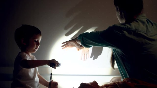 4k video of young mother showing shadows of animals on the bedroom wall with hands and flashlight before going to sleep with her toddler son