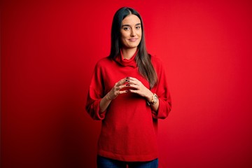 Young beautiful brunette woman wearing casual sweater over isolated red background Hands together and fingers crossed smiling relaxed and cheerful. Success and optimistic