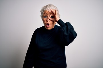 Senior beautiful woman wearing casual black sweater standing over isolated white background doing ok gesture shocked with surprised face, eye looking through fingers. Unbelieving expression.