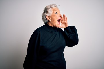 Senior beautiful woman wearing casual black sweater standing over isolated white background shouting and screaming loud to side with hand on mouth. Communication concept.