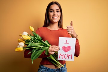 Beautiful woman celebrating mothers day holding love mom message and bouquet of tulips happy with big smile doing ok sign, thumb up with fingers, excellent sign