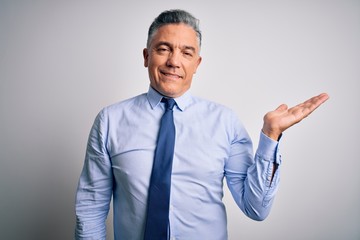 Middle age handsome grey-haired business man wearing elegant shirt and tie smiling cheerful presenting and pointing with palm of hand looking at the camera.