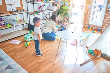 Beautiful teacher and group of toddlers playing around lots of toys at kindergarten