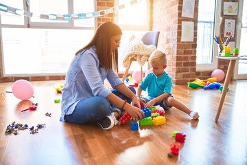 Young caucasian child playing at playschool with teacher. Mother and son at playroom bulding a...