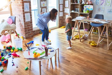 Young caucasian child playing at playschool with teacher. Mother and son at playroom around toys...