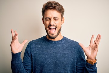 Fototapeta premium Young handsome man with beard wearing casual sweater standing over white background celebrating mad and crazy for success with arms raised and closed eyes screaming excited. Winner concept