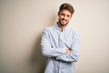Young handsome man with beard wearing striped shirt standing over white background happy face...