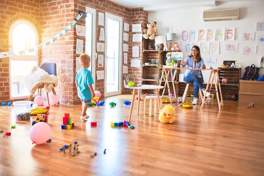 Young caucasian child playing at playschool with teacher. Young woman sitting on the desk of the classroom