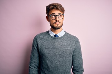 Young handsome man with beard wearing glasses and sweater standing over pink background smiling looking to the side and staring away thinking.