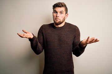 Young handsome blond man with beard and blue eyes wearing casual sweater standing clueless and...