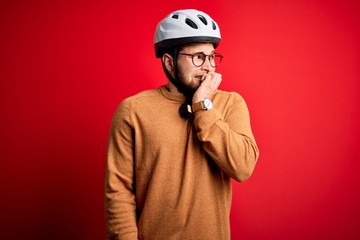 Young blond cyclist man with beard and blue eyes wearing bike helmet and glasses looking stressed and nervous with hands on mouth biting nails. Anxiety problem.
