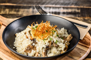 A serving of Mushroom Risotto in a dark round bowl on a wooden table.