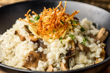 A serving of Mushroom Risotto in a dark round bowl on a wooden table.