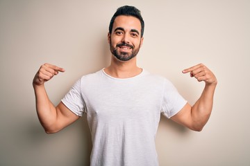 Young handsome man with beard wearing casual t-shirt standing over white background looking confident with smile on face, pointing oneself with fingers proud and happy.