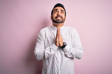 Young handsome man with beard wearing casual shirt standing over pink background begging and praying with hands together with hope expression on face very emotional and worried. Begging.