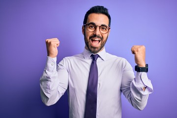 Handsome businessman with beard wearing casual tie and glasses over purple background celebrating surprised and amazed for success with arms raised and open eyes. Winner concept.