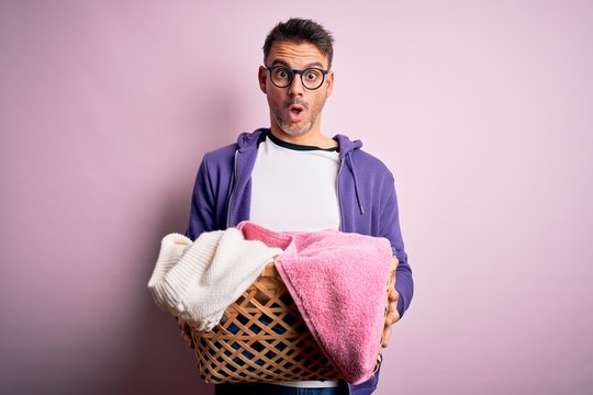 Young handsome man doing housework holding wicker basket with clothes scared in shock with a surprise face, afraid and excited with fear expression