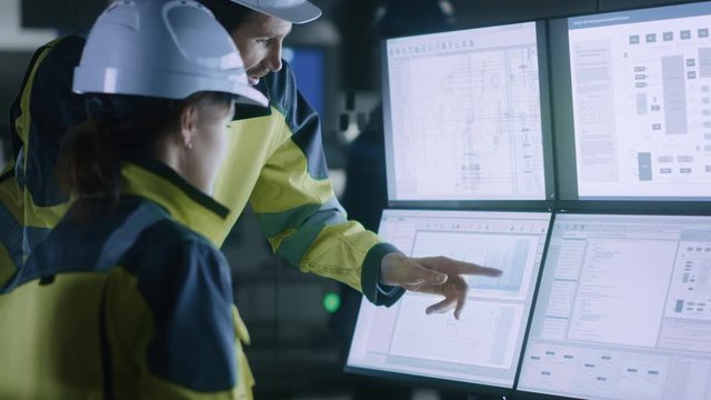 Industry 4.0 Modern Factory: Chief Project Manager Talks to Female Engineer, She Points at Computer Screens Showing Complex Industrial Electronics Design Blueprints, They Have Find Problem Solution
