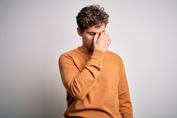 Young blond handsome man with curly hair wearing casual sweater over white background tired rubbing nose and eyes feeling fatigue and headache. Stress and frustration concept.