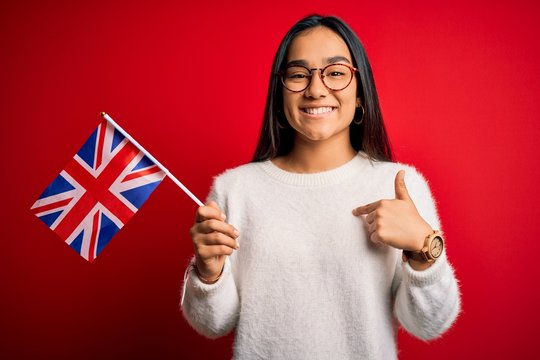 Young asian woman holding united kingdom flag for brexit referendum over red background with surprise face pointing finger to himself - Powered by Adobe