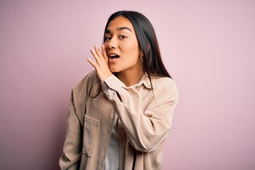 Young beautiful asian woman wearing casual shirt standing over pink background hand on mouth telling secret rumor, whispering malicious talk conversation