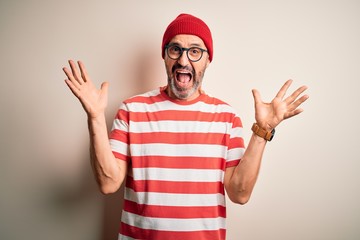 Middle age hoary man wearing striped t-shirt glasses and cap over isolated white background celebrating crazy and amazed for success with arms raised and open eyes screaming excited. Winner concept