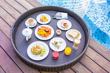 Flotaing breakfast tray around outdoor swimming pool with bread fruit egg coffee and juice