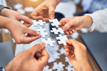 Group of business workers with hands together connecting pieces of puzzle at the office