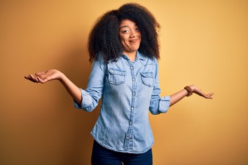 Young beautiful african american woman with afro hair standing over yellow isolated background...
