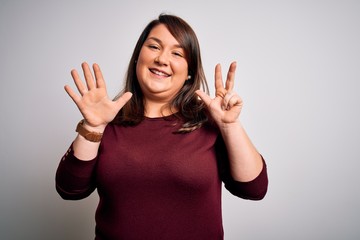 Beautiful brunette plus size woman wearing casual sweater over isolated white background showing and pointing up with fingers number eight while smiling confident and happy.