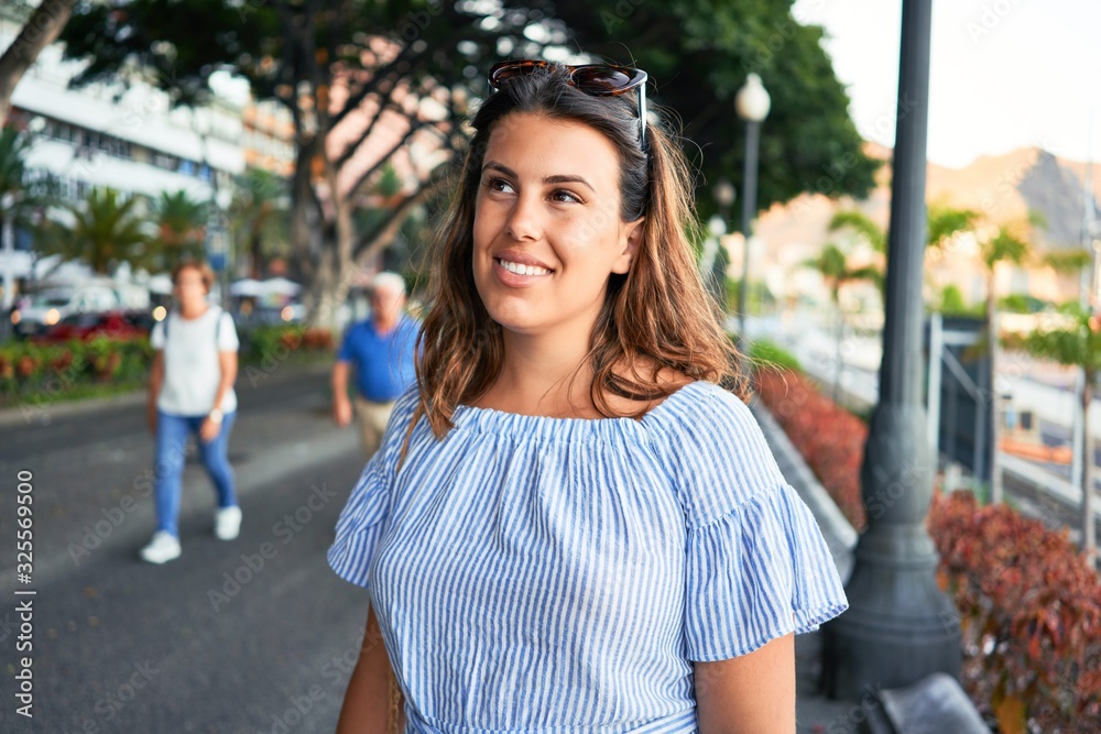 Wall mural Young beautiful woman smiling happy walking on city streets on a sunny day of summer