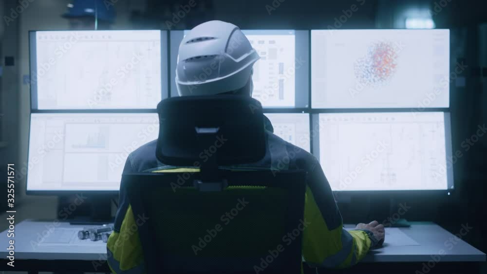 Poster Industry 4.0 Modern Factory: Facility Operator Wearing Hardhat and Safety Vest Controls Workshop Production Line, Uses Computer with Screens Showing Machinery Control Operation UI. Back View Zoom In