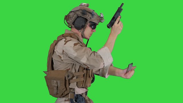 A special forces soldier with a helmet on his head walking and shooting from hand gun on a Green Screen, Chroma Key.