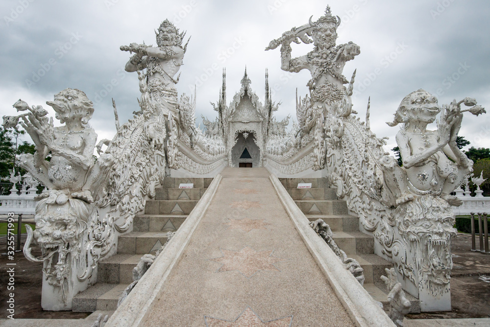 Wall mural Beautiful architecture of White temple (Wat Rong Khun)  in Chiang Rai province of Thailand in the cloudy day. The Wat Rong Khun was designed by Chalermchai Kositpipat, a famous Thai visual artist.