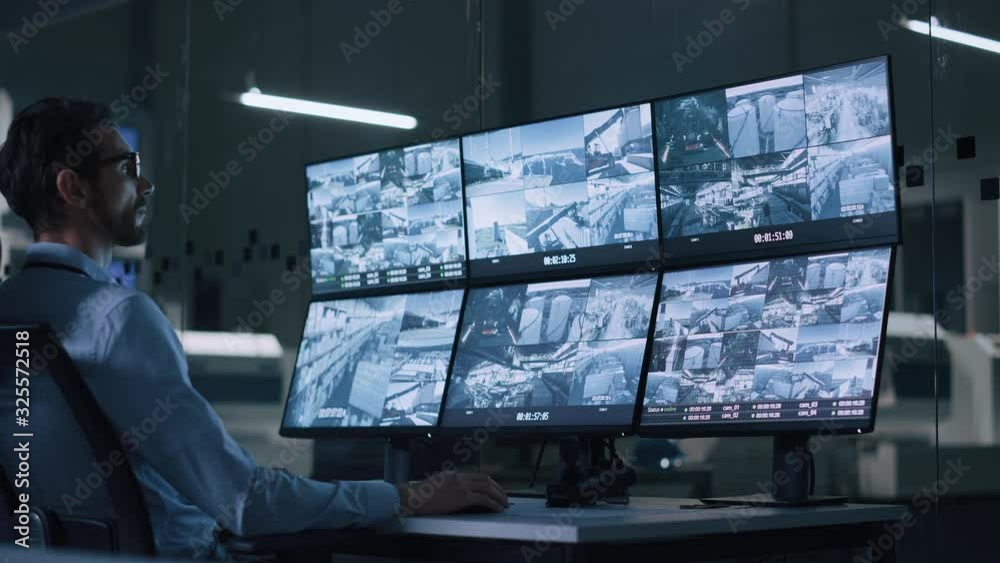 Aufkleber Industry 4.0 Modern Factory: Security Operator Controls Proper Functioning of Workshop Production Line, Uses Computer with Screens Showing Surveillance Camera Footage Feed. High-Tech Security