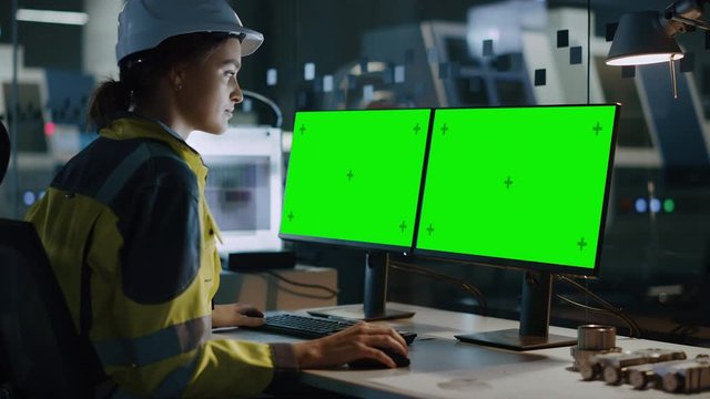 Female Engineer Wearing Safety Vest and Hardhat Works on a Computer, Two Monitor Screens Show Chroma Key / Green Screen Displays. Modern High-Tech Industry 4.0 Electronics Production Factory
