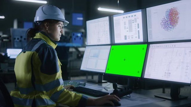Industry 4.0 Modern Factory: Confident Female Operator Controls Facility, Uses Computer with Multiple Screens Including: Green Screen / Chroma Key, AI Concept, Machine Learning UI
