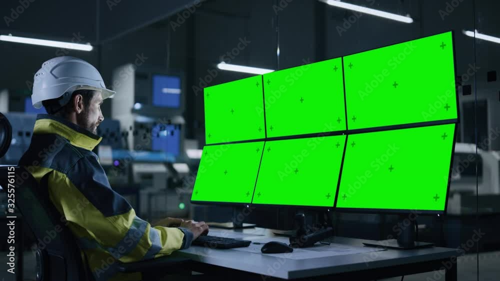 Poster Industry 4.0 Modern Factory: Handsome Male Operator Controls Facility, Uses Computer with Multiple Chroma Key / Green Screen Displays. In Background Dark Automated Electronics Producing Facility
