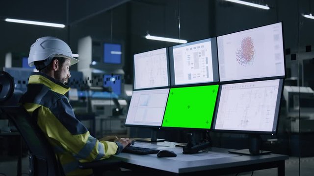 Industry 4.0 Modern Factory: Handsome Male Operator Controls Facility, Uses Computer with Multiple Screens Including: Green Screen / Chroma Key, AI Concept, Machine Learning UI