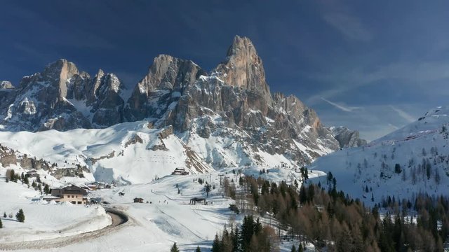 Stunning view of Passo Rolle - a high mountain pass in Trentino in Italy. A narrow road meandering on the slopes. A spiky crown of mountain peaks towering over the snow-covered plateau.