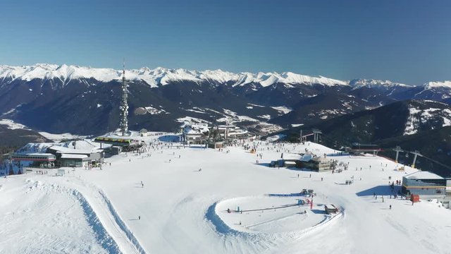 Aerial view of the Kroplatz mountain top, a famous skiing resort in Italy. Concordia bell is ringing, skiers ride on the plateau. It is sunny, the sky is clear, the valley below is covered with snow.