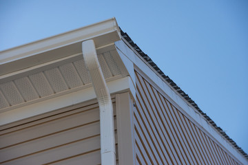 White Vinyl Downspout gutter system and gutter guard running along  beige horizontal sidings with soffit  providing ventilation on a brand new US single family home © tamas