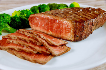 Medium rare beef sirloin with broccoli on white plate.