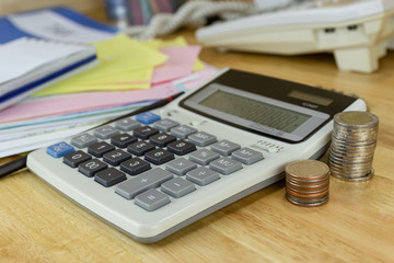 the stack of coin with calculator on wood table at office, concept of calculating expenses, incomes and expenses.