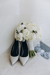 white women’s shoes and a wedding bouquet stand against a white wall