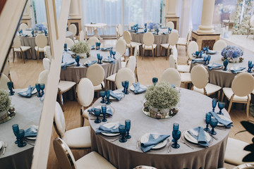 festive tables in the banquet room are decorated with compositions of white and blue flowers, on the tables are plates with napkins, glasses, candles, a wedding dinner